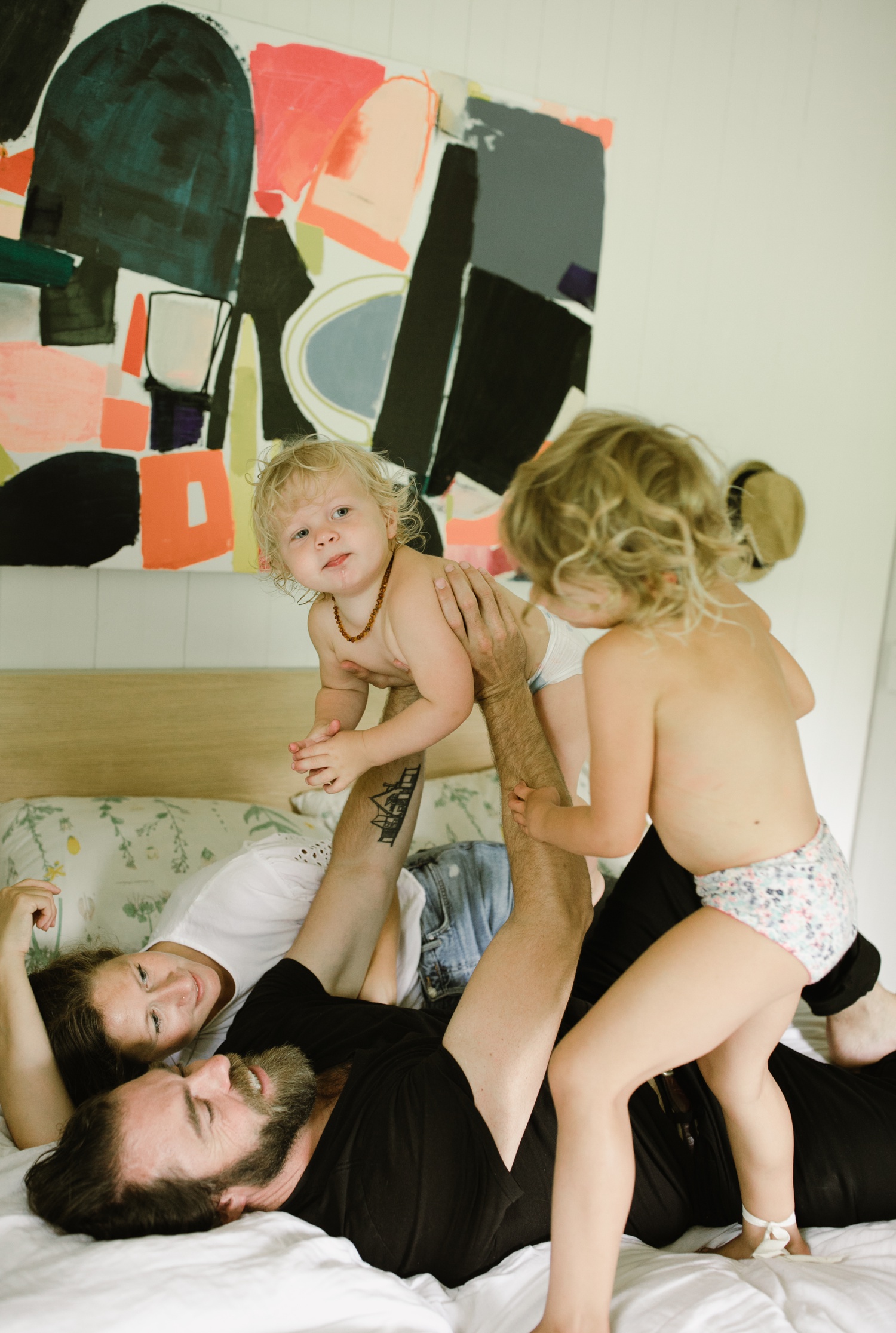 Family portraits on a bed with a piece of abstract art hanging above it