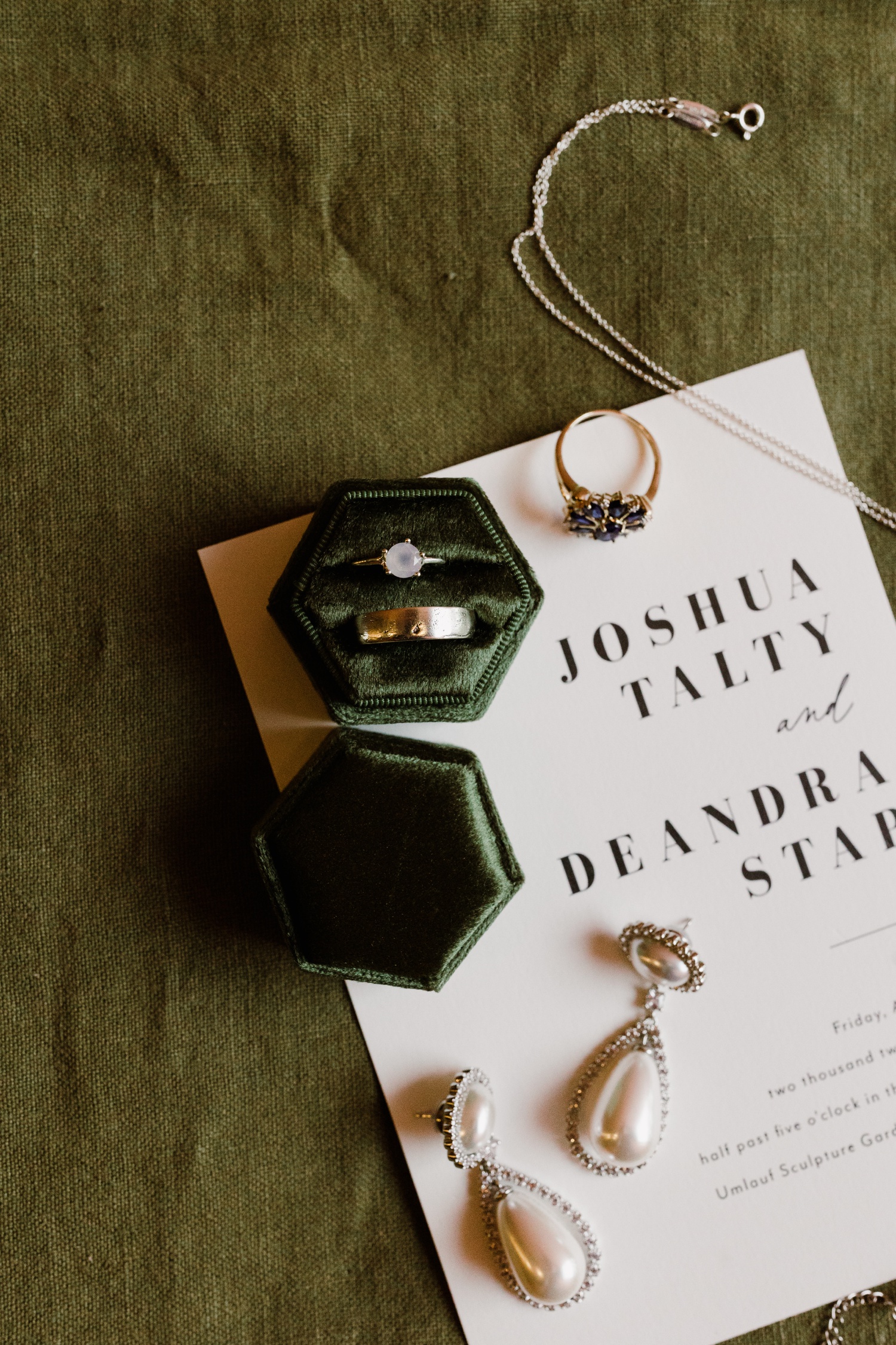 Flatlay of a modern wedding invitation with a green velvet ring case and pearl drop earrings
