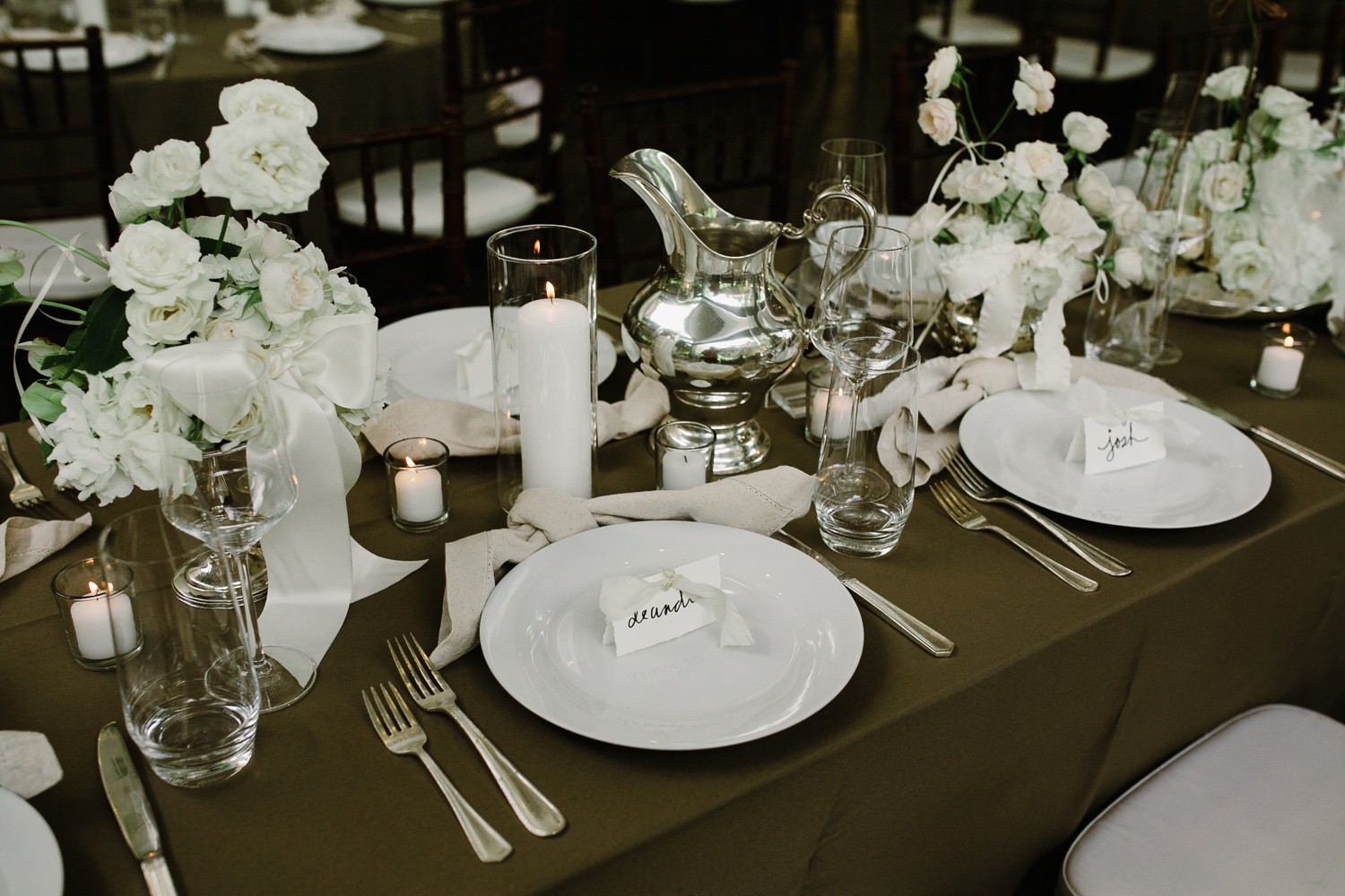 Spring wedding tablescape with an olive green tablecloth and white flowers