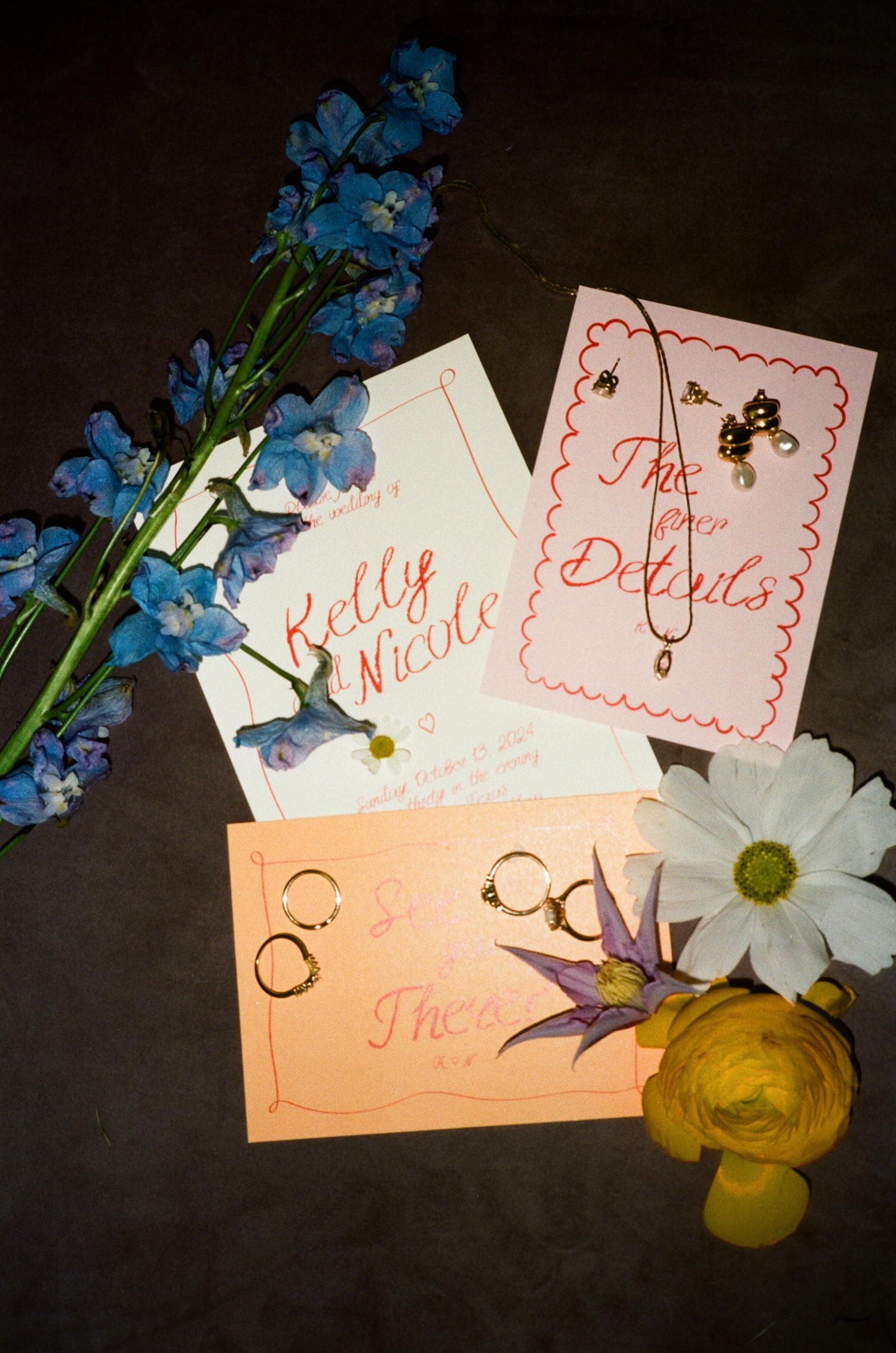 A film photo of a colorful flat lay with flowers, wedding invitations, and gold jewelry