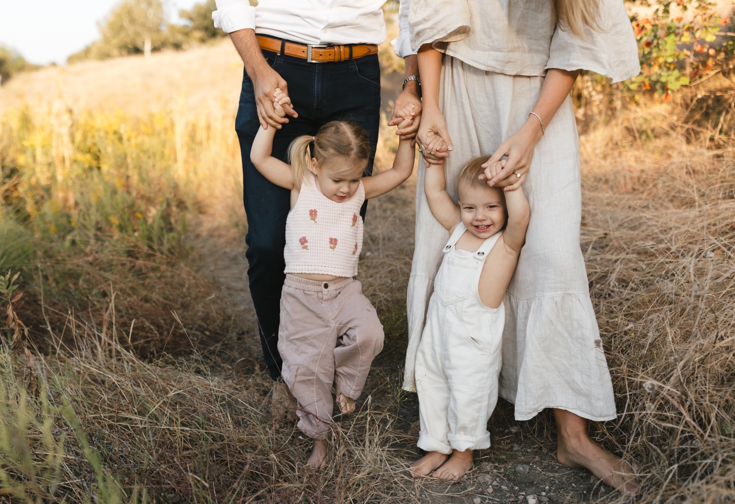 A mother and father holding the hands of their young daughter and son