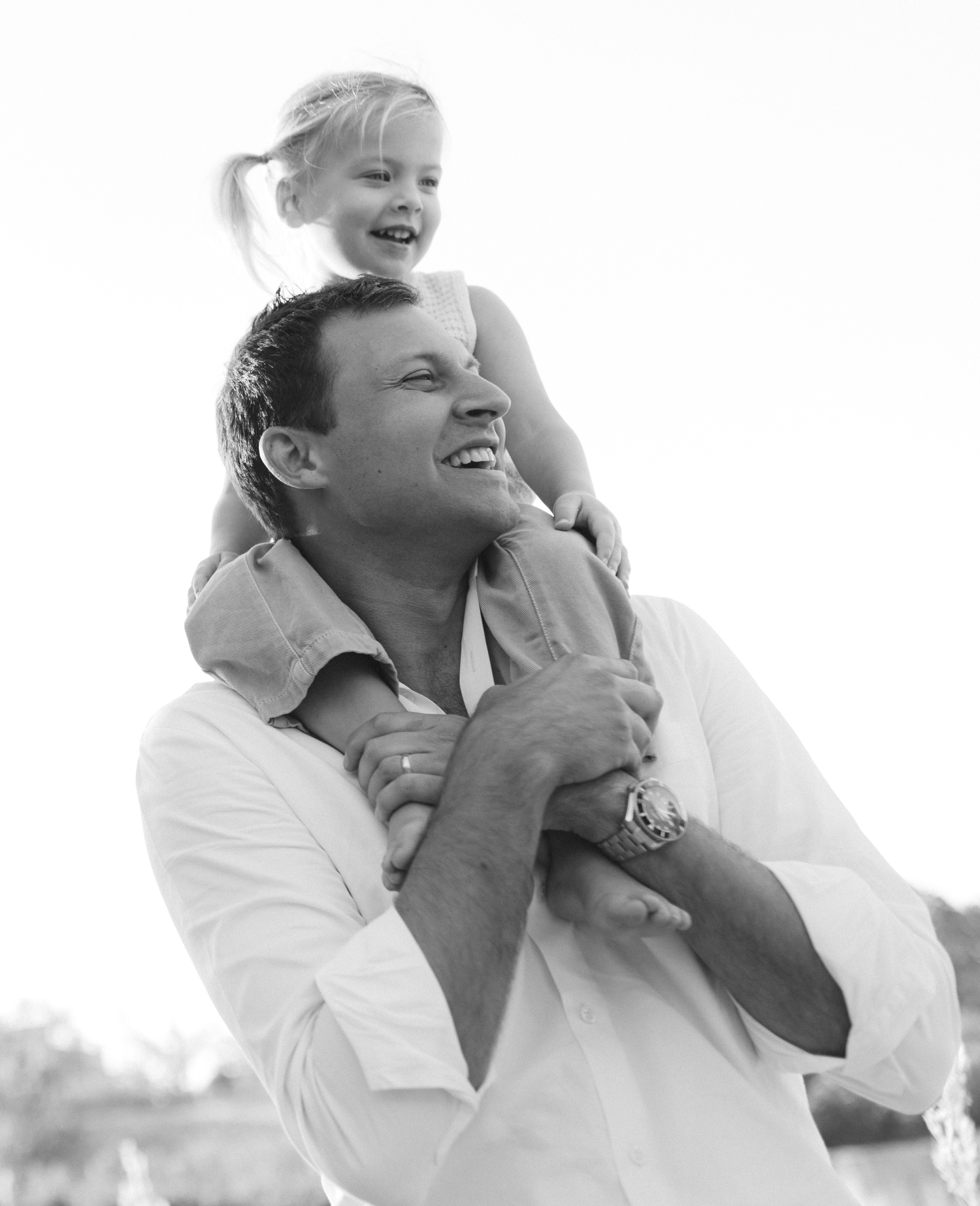 A black and white portrait of a father with his daughter on his shoulders 