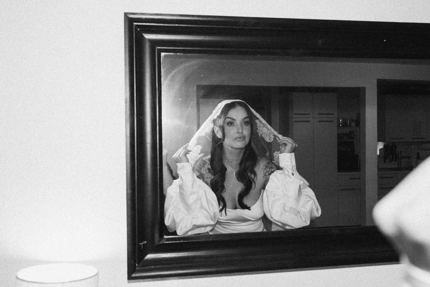 A black and white film photo of a bride fixing her veil before her wedding ceremony