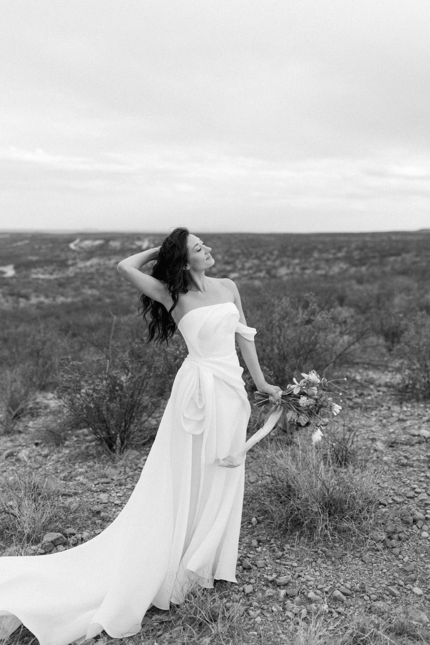 Black and white portrait of a bride running a hand through her hair and holding a bridal bouquet