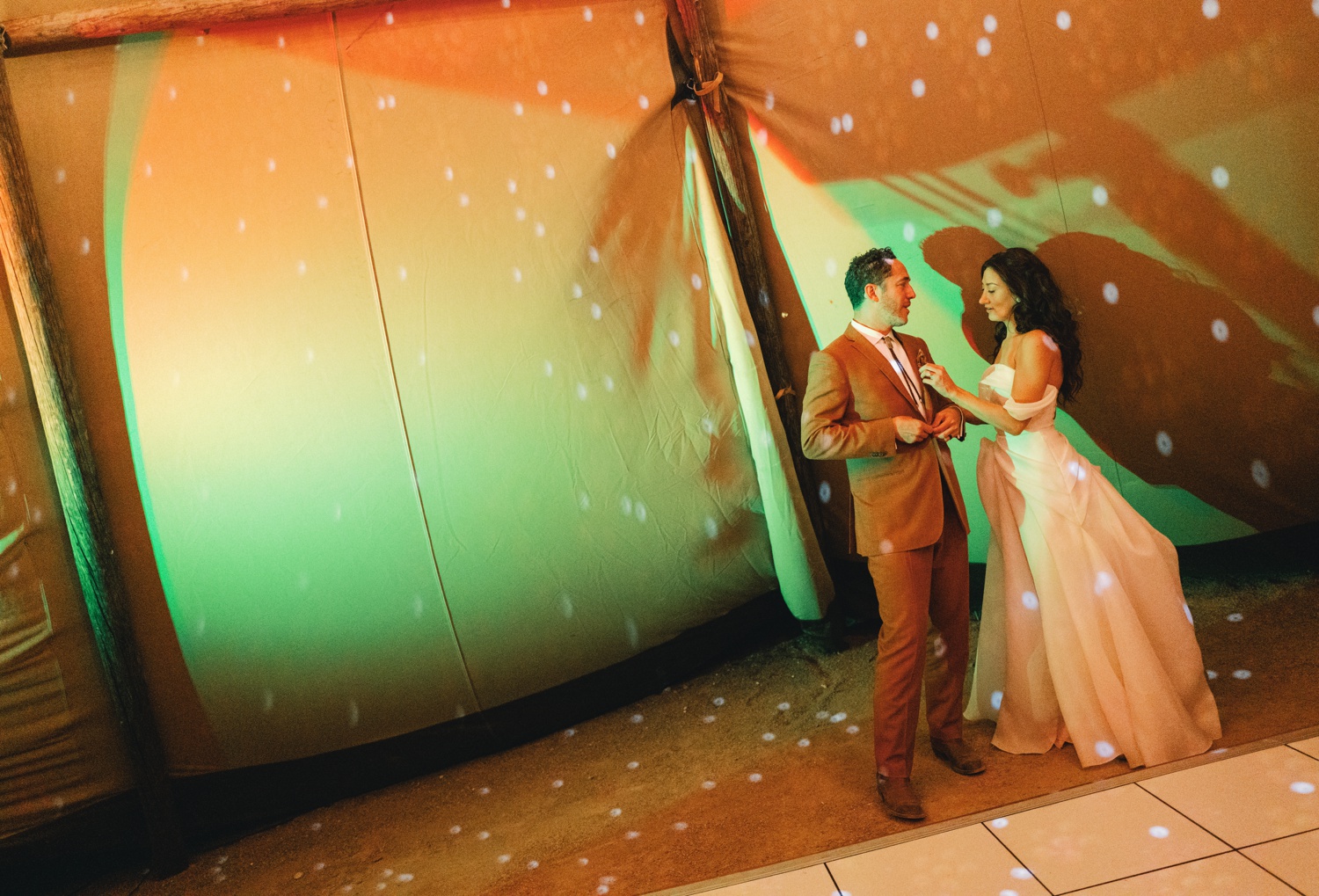 Bride and groom dancing in a tent with multi-colored lights
