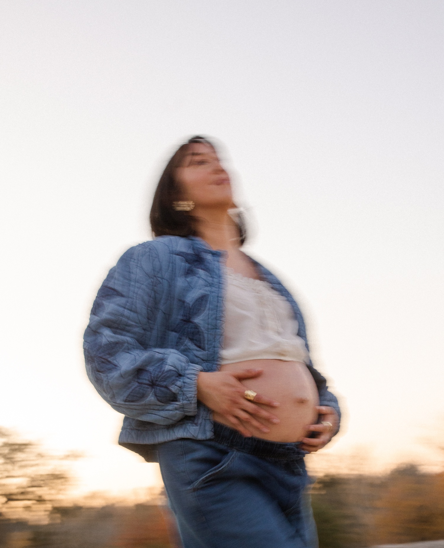 Blurry film photo of a pregnant woman wearing a Free People quilted jacket and cradling her baby bump