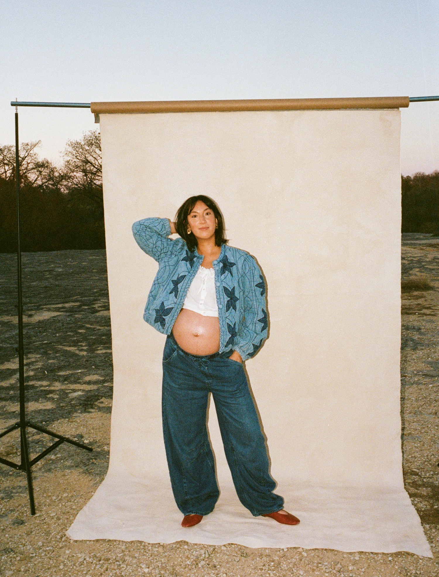 Pregnant woman wearing baggy jeans, a cropped peasant blouse, and a Free People quilted jacket for an outdoor photoshoot