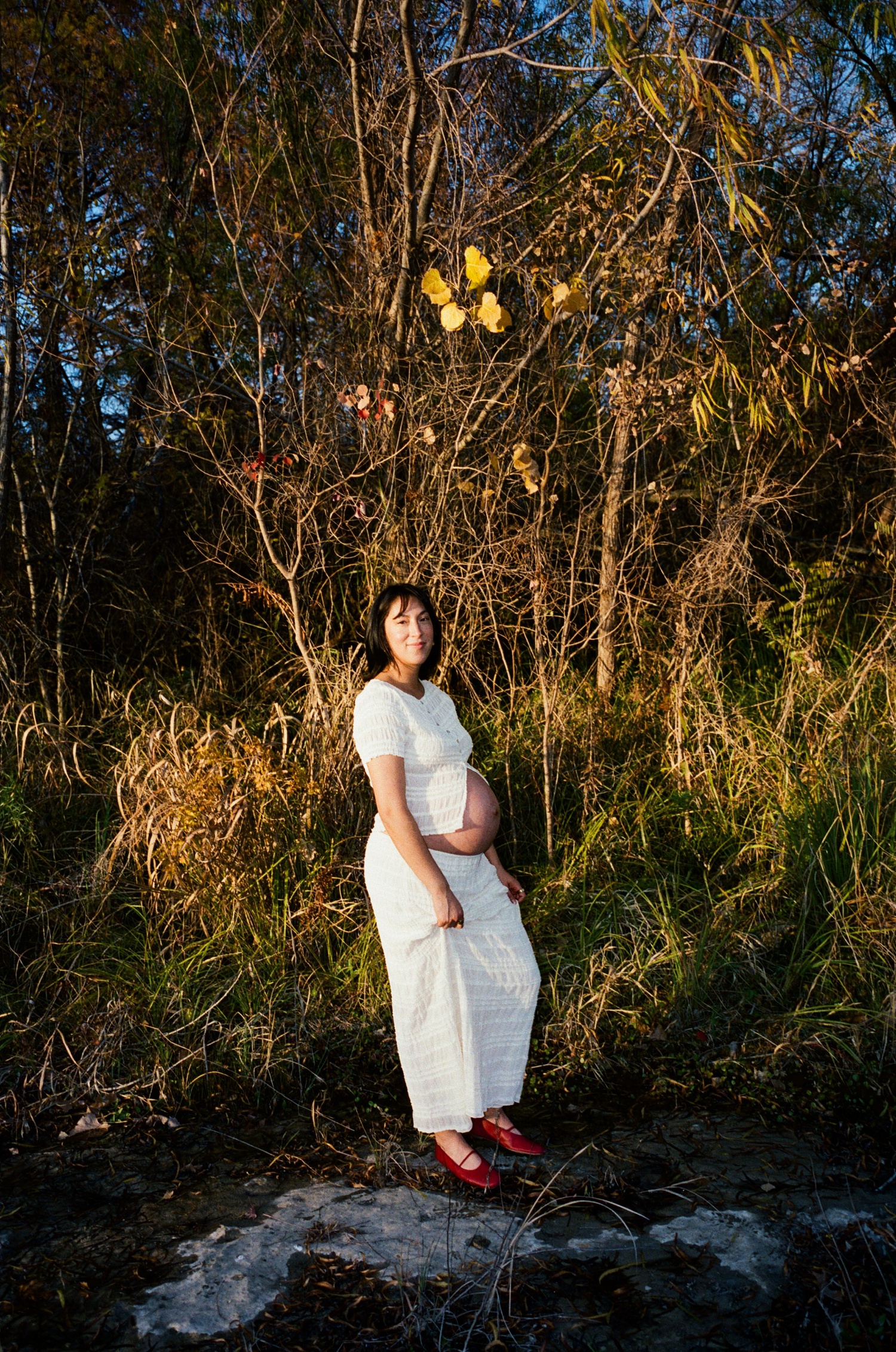 Pregnant woman wearing a white two-piece set and red ballet flats for an outdoor photoshoot